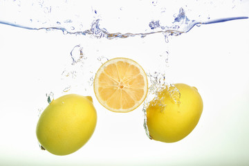 Two lemons and lemon slice spash in water on white