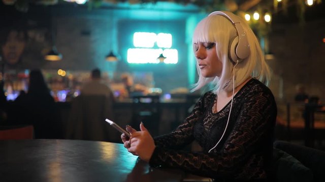 Unusual blonde girl listening to music in a bar using headphones