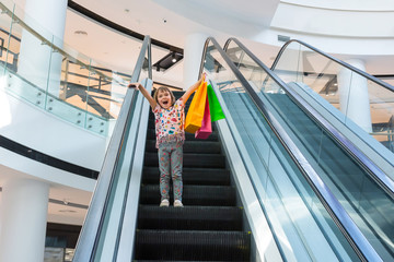 The happy child with purchases in shopping center on the escalator
