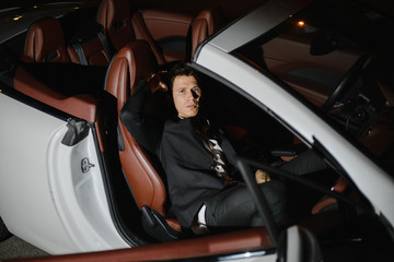 Fototapeta na wymiar Portrait of a handsome man in white cabriolet. Nightlife. Businessman in suit in luxury car