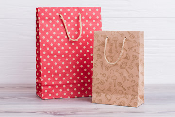 Two natural paper shopping bags. Red and brown paper gift bags with printing on light wooden...