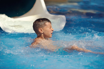 Boy havimg fun at waterpark.  He just dived in waterpark pool after from sliding flume.