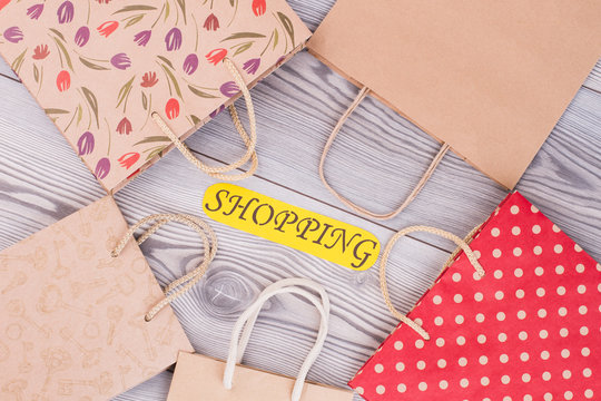 Paper bags and card with inscription shopping. Set of kraft paper packets on wooden background. Holiday shopping concept.