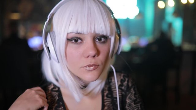 Unusual blonde girl listening to music in a bar using headphones
