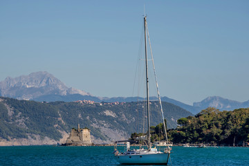 Beautiful sailing boat anchored in the Gulf of poets with the Torre Scola or Scuola or torre di San Giovanni Battista  in the background, Portovenere, Liguria, Italy