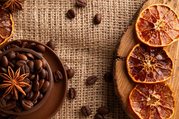 High contrast photo of dried oranges, Arabica and Robusta beans in a stein on a saucer with anise. View from above. Photo on a gray textured canvas burlap.