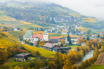 Fototapeta na wymiar Picturesque autumnal view on Novacella, Varna, Bolzano in South Tyrol. Mountain scenery in Northern Italy. View from the top on the mountain valley. Colourful vineyards and yellow foliage on trees.