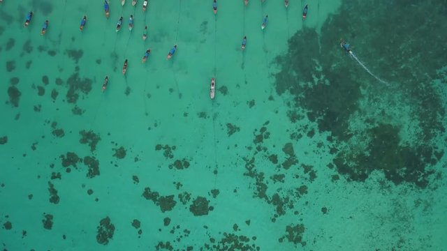 Top of traditional Thai boats, white sand beach, beautiful clear emerald sea, seen from camera down forward moving high aerial drone view on tropical island, Ko Lipe, Thailand.