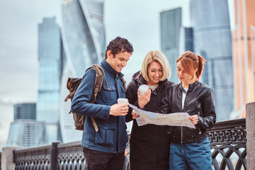 Fototapeta premium Group of happy tourists searching place on the map in front of skyscrapers