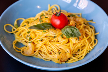 Close up of yellow spaghetti with prawns in a blue plate.