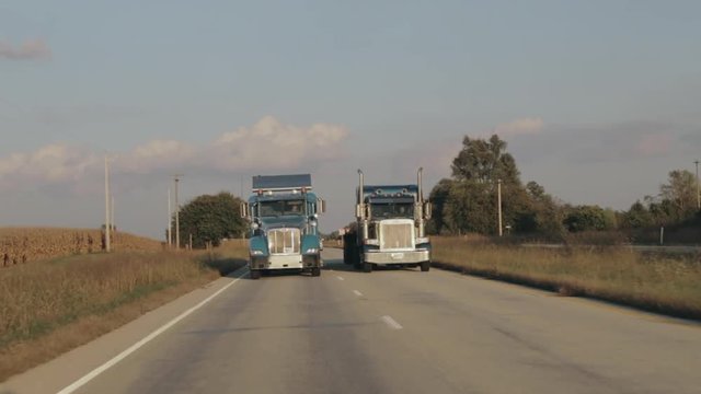 Two Peterbilt semi eighteen wheeler trucks driving down the highway in evening sun side by side