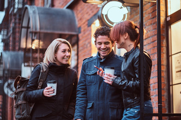 Three friends students having a break with coffee near a cafe outside.
