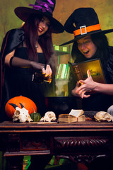 Photo of two witches brunettes in black hats brewing potion
