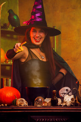 Image of young witch in black hat with outstretched hand with magic wand and cauldron