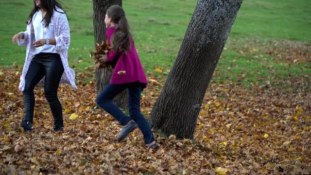 Mom and her little daughter are having fun in the autumn forest. They jump and throw leaves into the air. They are laughing. The family is happy.