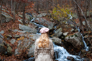 Fototapeta na wymiar Travel concept. Beautiful woman is looking at waterfal in autumn forest.