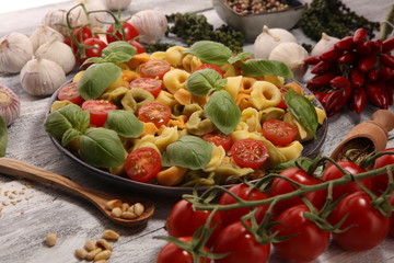 pasta. tricolor tortellini pasta salad with tomatoes and onions on wood table background.