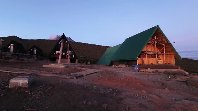Static shot of people walking, between cottages in a small town, on mount Kilimanjaro, on a colorful evening, in Tanzania, Africa