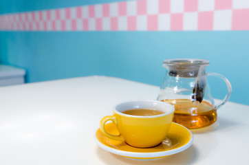 Yellow cup of tea and glass teapot on the table. Blue background