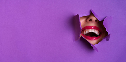 View of bright lips through hole in violet paper background. Make up artist, beauty concept....