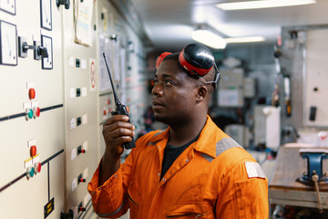 African marine engineer officer in engine control room ECR. He speaks with VHF or UHF portable radio. Ship communication routine