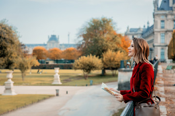 Style redhead girl in red coat with map looking at park in Paris. Autumn season time