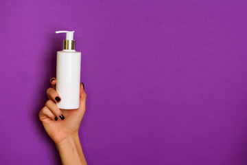 Female hands holding white cosmetic bottle on violet background. Banner. Skin care, pure beauty,...