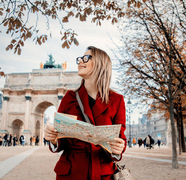 Style redhead girl in red coat and bag with map in parisian park in autumn season time