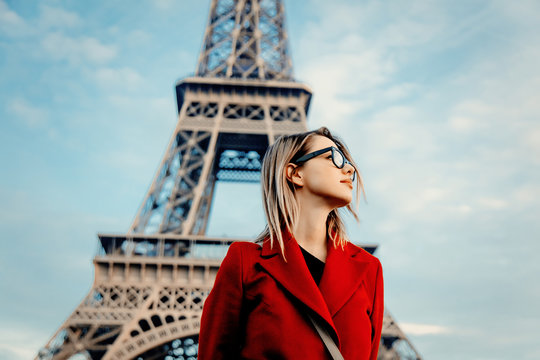 Style redhead girl in red coat and bag at parisian street with view at Eiffel tower in autumn season time