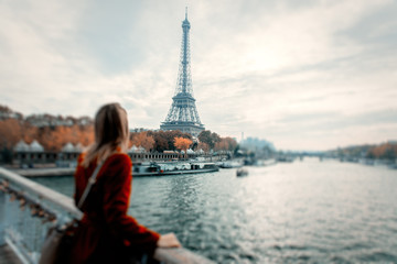 Style redhead girl in red coat and bag at parisian street with view at Eiffel tower in autumn season time