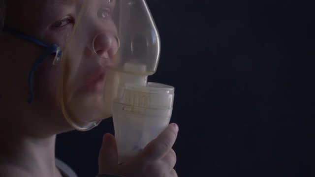 Caucasian blond child is crying from spasm of bronchitis and inhales vapors containing medications from inhaler to stop choking. Medical procedures. Respiratory medicine. Bronchitis, asthmatic problem