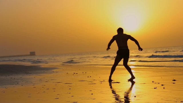 Muay thai fighter without t-shirt is doing shadow boxing on the beach during sunset