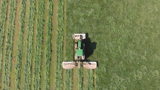 Aerial top down shot above tractor mowing grass stripes into field.