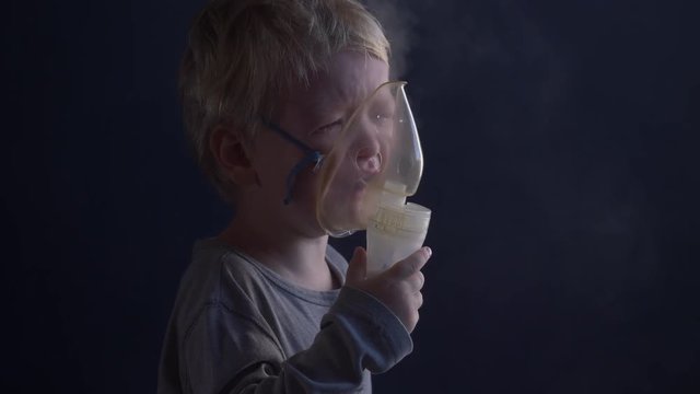 Caucasian blond child is crying from spasm of bronchitis and inhales vapors containing medications from inhaler to stop choking. Medical procedures. Respiratory medicine. Bronchitis, asthmatic problem