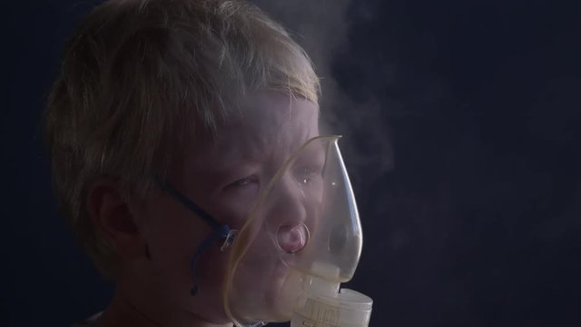 Caucasian blond child is crying from spasm of bronchitis and inhales vapors containing medications from inhaler to stop choking. Medical procedures. Respiratory medicine. Bronchitis, asthmatic problem