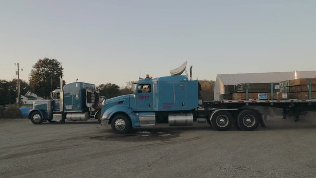 Two Peterbilt Semi Trucks parking at truck yard with lumber load on flatbed trailer