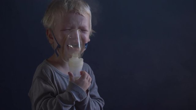 Caucasian blond child is crying from spasm of bronchitis and inhales vapors containing medications from inhaler to stop choking. Medical procedures. Respiratory medicine. Bronchitis, asthmatic problem