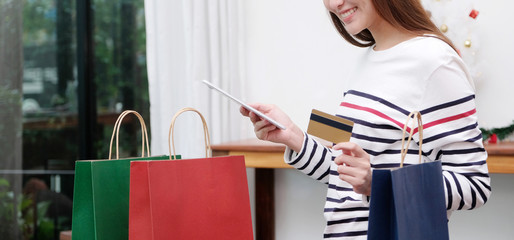 Women holding digital tablet and credit card for Christmas shopping online while standing at home, Christmas holiday shopping concept
