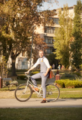 one young man, 20-29 years old, wearing hipster suit, sitting posing on a old retro city bike outdoors, on sunny day, in park.