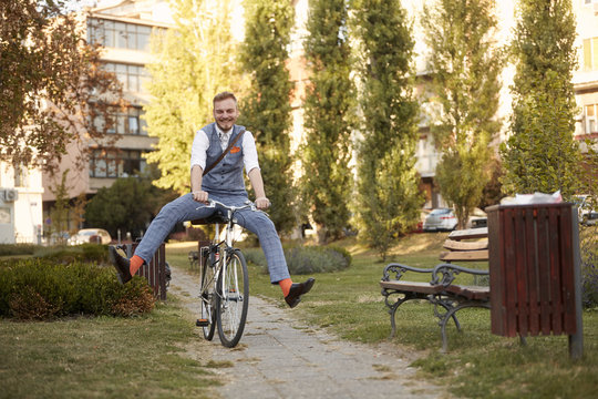 One Young Man, 20-29 Years Old,  Wearing Hipster Suit, Smart Casual, Ridiculous Funny Riding Bike (legs Spread) In Park Road Trail.