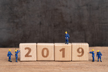 New year 2019 begin concept, cute miniature people worker staffs finish building cube wooden block as year number 2019 on wood table with dark blackboard background with copy space