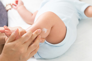 Mother is applying cream to the baby boy which helps to maintain skin leg hydration, Skincare and moisturizing cream concept - obrazy, fototapety, plakaty