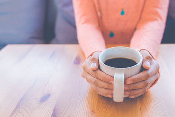Woman hand in warm sweater holding a cup of coffee.