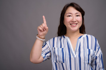 Mature beautiful Asian businesswoman against gray background