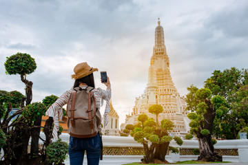Asian woman tourists are taking photos With a smartphone at the Wat Arun temple on vacation Bangkok Thailand.