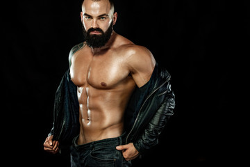 Fototapeta na wymiar Men fashion concept. Close-up portrait of a brutal bearded man topless in a leather jacket. Athlete bodybuilder on black background.