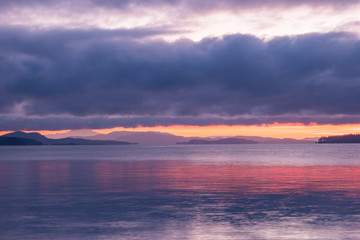 Obraz premium glowing orange and pink sky behind island near sunrise with heavy cloud covering the sky