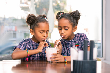 Waiting parents. Stylish cute siblings wearing bright bracelets drinking cocktail together waiting for their parents