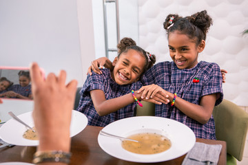 Posing for photo. Two cute dark-eyed daughters having fun while posing for photo sitting in front of their mother