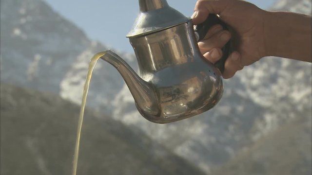 A tracking shot of a glass of mint tea being poured with the Atlas Mountains as a backdrop